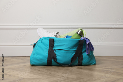 Blue gym bag with sports accessories on floor near white wall indoors photo