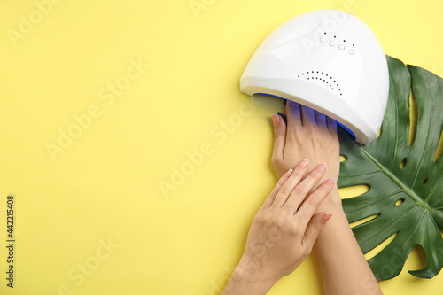 Woman using ultraviolet lamp to dry gel nail polish on yellow background, top view. Space for text