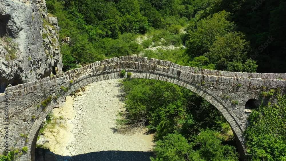 Drone flying over very old, ancient stone bridge in Kokkinou, Greece. There are people walking on the path underneath the bridge. It is a sunny summer day. Drone aerial 4K stock footage Drone flying over very old, ancient stone bridge in Kokkinou, Greece. There are people walking on the path underneath the bridge. It is a sunny summer day. Drone aerial 4K stock footage