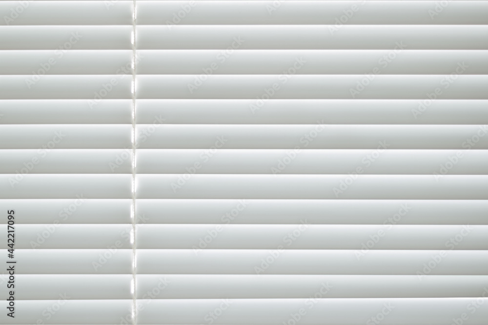 Frontal view of white office shutters made of metal. The strips are arranged horizontally, on the left there is a thread for opening the curtains. Texture, background and copy space. Frontal view of white office shutters made of metal. The strips are arranged horizontally, on the left there is a thread for opening the curtains. Texture, background and copy space.
