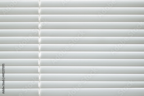 Frontal view of white office shutters made of metal. The strips are arranged horizontally, on the left there is a thread for opening the curtains. Texture, background and copy space.