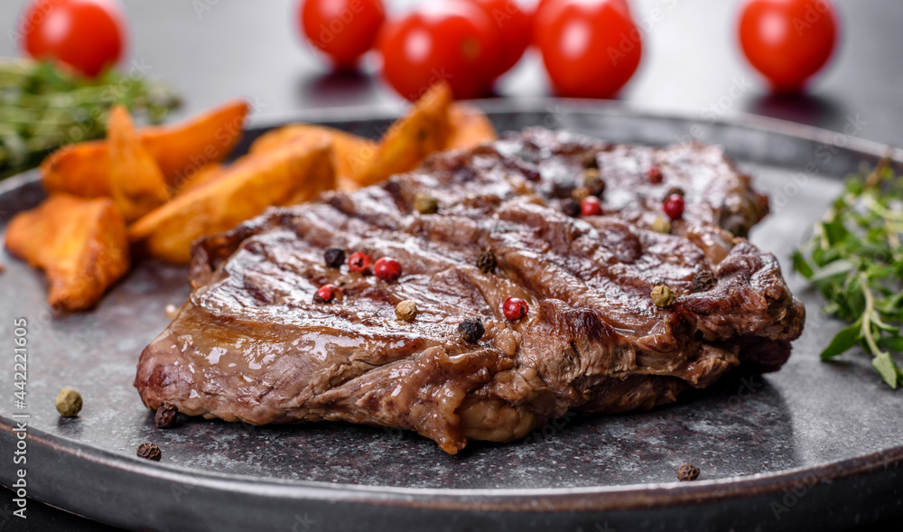 Delicious juicy fresh beef steak with spices and herbs on a dark concrete background