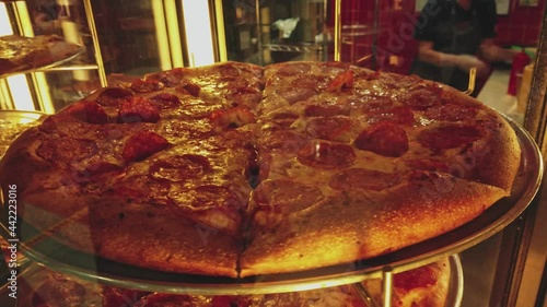 Fresh made pepperoni pizza on turntaible in store pizzeria window. Stuff is moving on background.