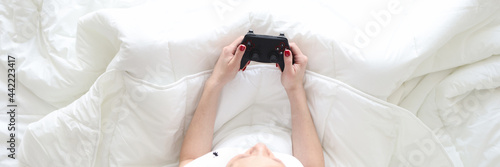 Woman sitting in bed with joystick in her hands top view