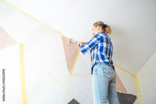 Young happy woman painting interior wall with paint roller in new house, Home decoration concept