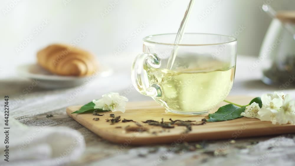 Jet of green jasmine tea flows in glass cup. Transparent cup on bamboo board with jasmine sprigs is filled tea. Background fresh croissant on dish Breakfast with tea and croissant on a sunny morning.
Jet of green jasmine tea flows in glass cup. Transparent cup on bamboo board with jasmine sprigs is filled tea. Background fresh croissant on dish Breakfast with tea and croissant on a sunny morning.