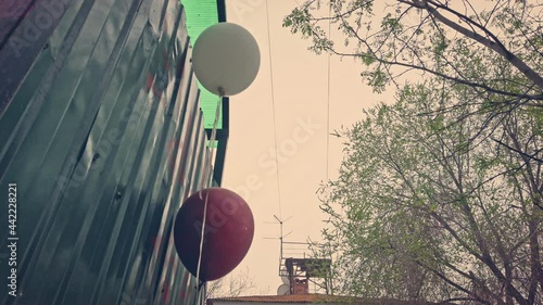 Depression, party is over. Red and white balloons set near trash dumpsters of a ghetto.