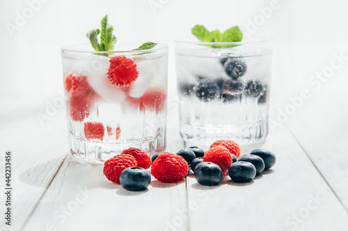 Summer drinks. Refreshing water or soda with ice and berries in a beautiful glass stands on a white wooden table. Seasonal drinks and cocktails