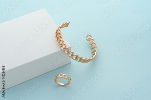 Chain shape gold bracelet and ring on white box on blue background with copy space