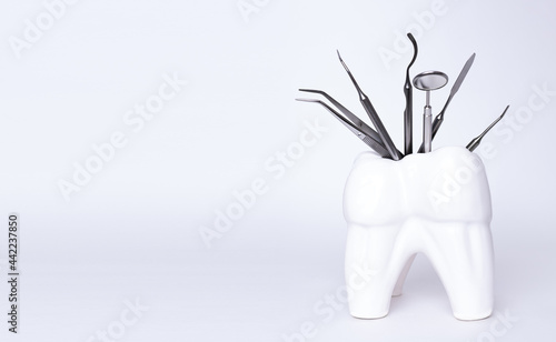 Dental professional steel tools in tooth shaped holder on grey background. Set of metal medical equipment tools for teeth dental care. sickle probe, dental explorer, mirror, burnisher, forceps