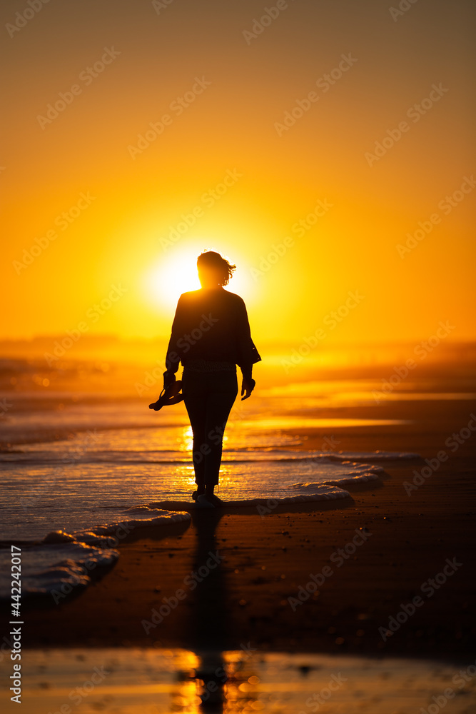 Silueta de mujer caminando por la playa al ocaso en vacaciones