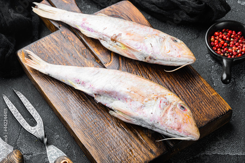 Raw fresh mullet or barabulka whole fish, with ingredients and herbs, on black dark stone table background