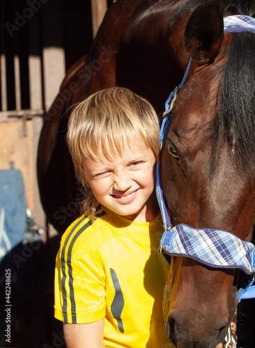 happy portrait of little boy with horse posing in stable. sunny day