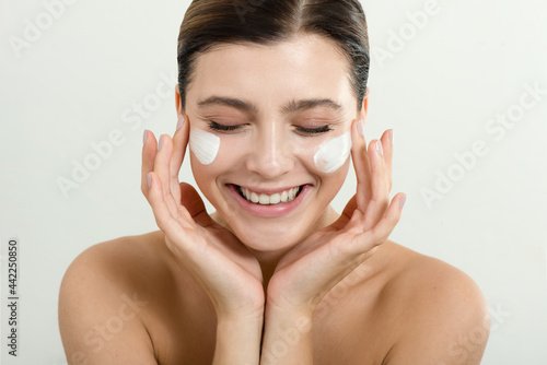 Young woman applying face cream on her face. Beauty model with perfect fresh skin and long eyelashes cares about her skin at home. Spa and Wellness, Skin Care Concept.