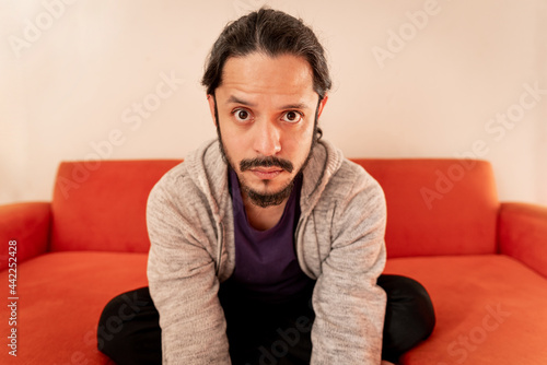 Young latin man portrait sitting on a couch sofa at home in the living room © Angel Gruber