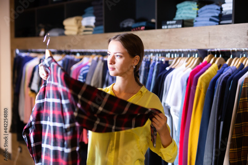 Satisfied woman chooses fashionable checkered shirt in the fashion store