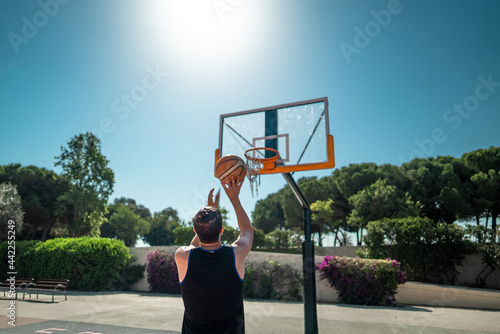 Male sportsman playing basketball throwing the ball at playground, rear view