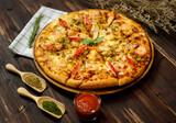 Selective focus and close up on homemade seafood pizza with shrimp, pineapples, bell pepper, crab sticks on wooden tray and table decorated with tomato sauce or ketchup, dried plants and oregano.