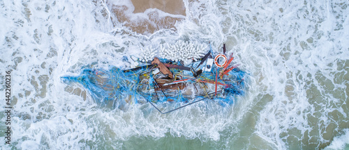 Broken boat and fishing nets washed up on a beach fish shape water sand debris waste plastic wood environmental global warming concept