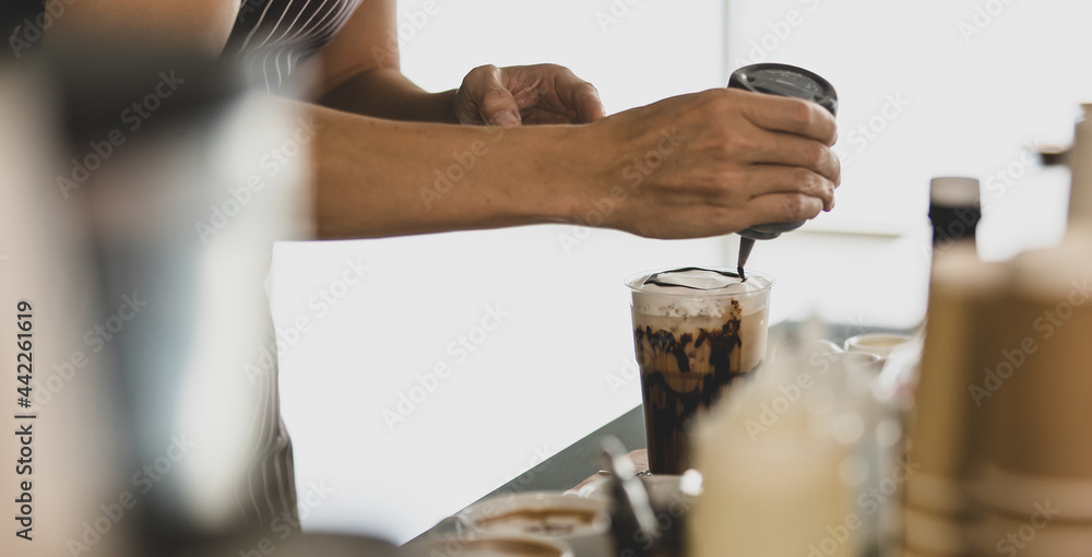 Unrecognizable barista man smiles and happy as enjoy decorating creamy foam of cold drinks in plastic cup with elaborate by squeezing bottle to pour chocolates on it Unrecognizable barista man smiles and happy as enjoy decorating creamy foam of cold drinks in plastic cup with elaborate by squeezing bottle to pour chocolates on it