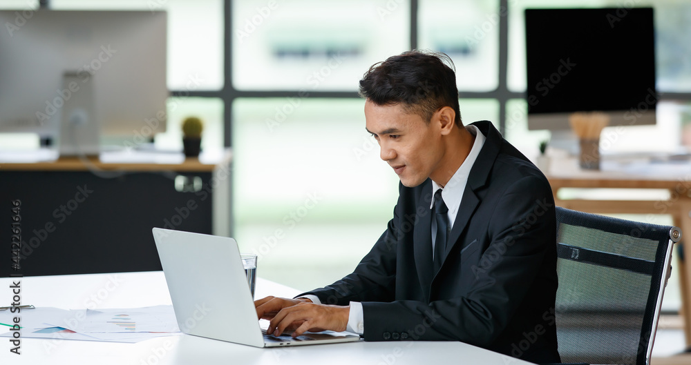 Cheerful businessman typing on laptop in office Cheerful businessman typing on laptop in office