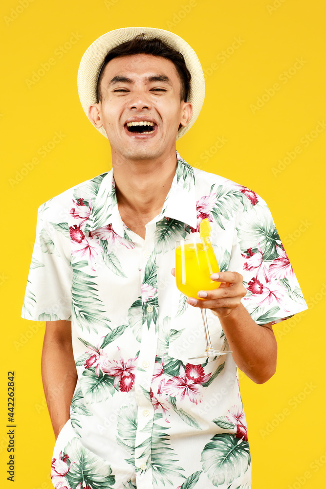 Young attractive Asian man in white Hawaiian shirt holding a glass of orange juice against yellow background. Concept for beach vacation holiday Young attractive Asian man in white Hawaiian shirt holding a glass of orange juice against yellow background. Concept for beach vacation holiday