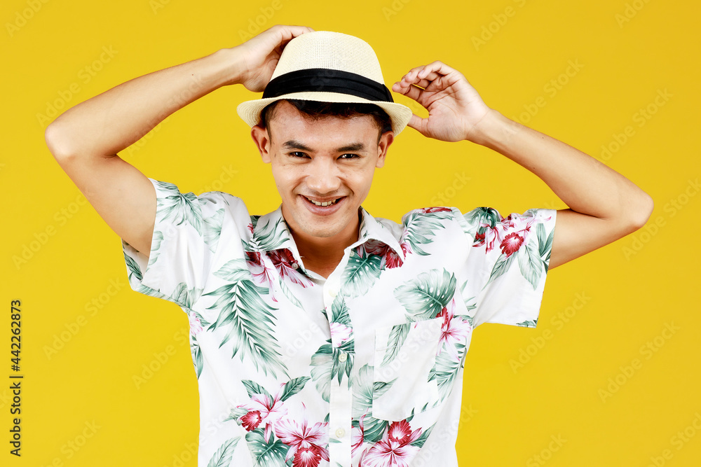 Young attractive Asian man in white Hawaiian shirt wearing white hat relaxing against yellow background. Concept for beach vacation holiday Young attractive Asian man in white Hawaiian shirt wearing white hat relaxing against yellow background. Concept for beach vacation holiday