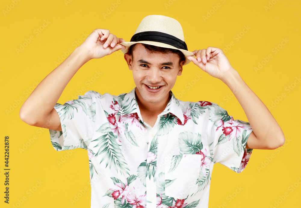 Young attractive Asian man in white Hawaiian shirt wearing white hat relaxing against yellow background. Concept for beach vacation holiday
