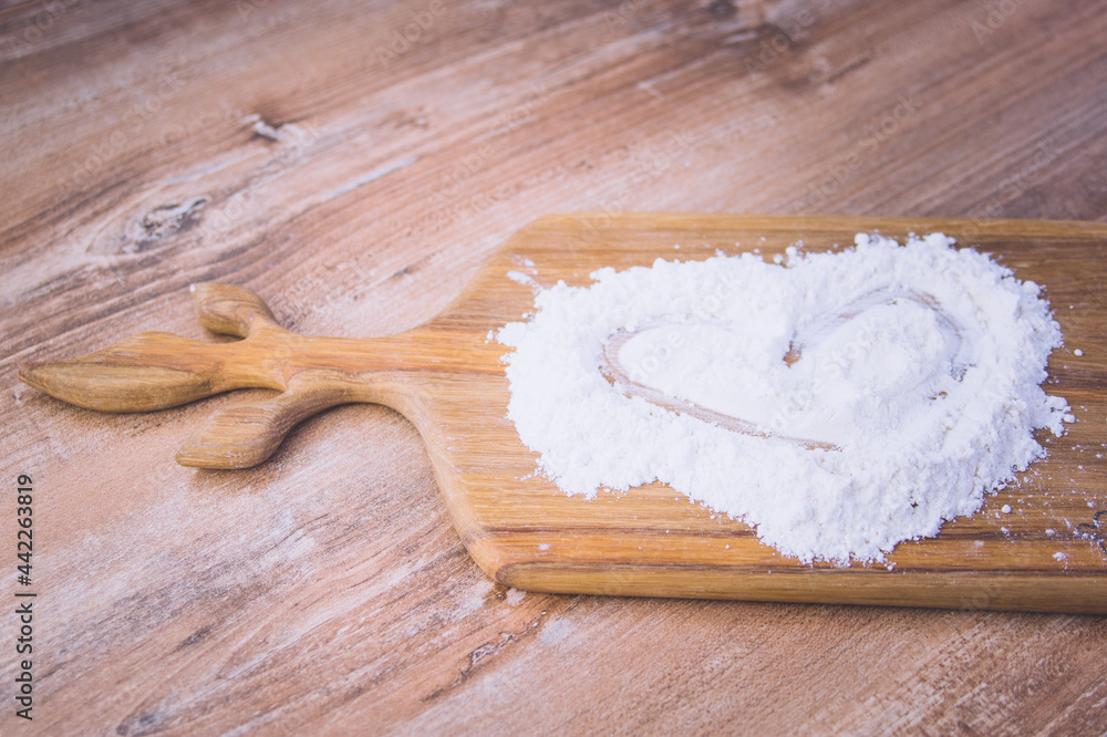 sprinkled wheat flour with a painted heart on a wooden board and wooden table sprinkled wheat flour with a painted heart on a wooden board and wooden table