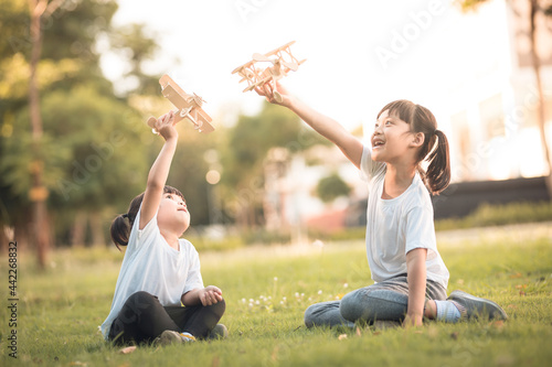 Fototapeta Naklejka Na Ścianę i Meble -  Two little kids playing with cardboard toy airplane in the park at the day time. Concept of happy game. Child having fun outdoors.