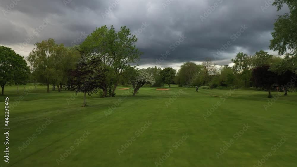 Climactic overcast over a golf field with trees on the finely cut grass. A rainstorm in the background. Sandpits Climactic overcast over a golf field with trees on the finely cut grass. A rainstorm in the background. Sandpits