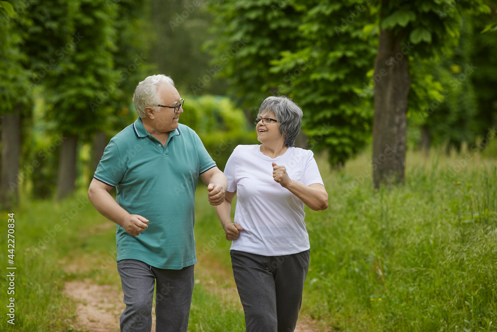 Portrait of two happy senior people on their morning run in a green park or forest in the countryside. Energetic old man and woman in their 60s enjoying sports exercise and running workout in nature Portrait of two happy senior people on their morning run in a green park or forest in the countryside. Energetic old man and woman in their 60s enjoying sports exercise and running workout in nature