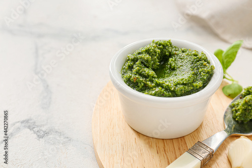 Wooden board with bowl of fresh pesto sauce and ingredients on light table