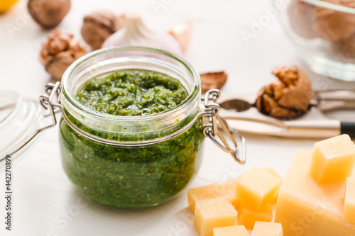 Jar with fresh pesto sauce and cheese on light wooden table