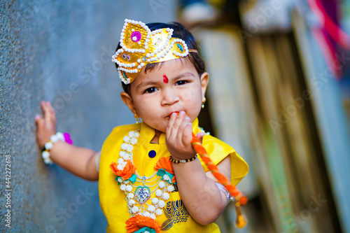 happy Janmashtami Greeting Card showing Little Indian boy posing as Shri krishna or kanha kanhaiya with Dahi Handi picture and colourful flowers.