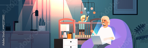 busy father freelancer working at home using laptop little son playing with toys in crib freelance fatherhood concept