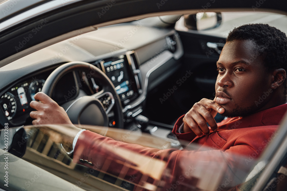 Pensive african business man inside of car holding wheel
