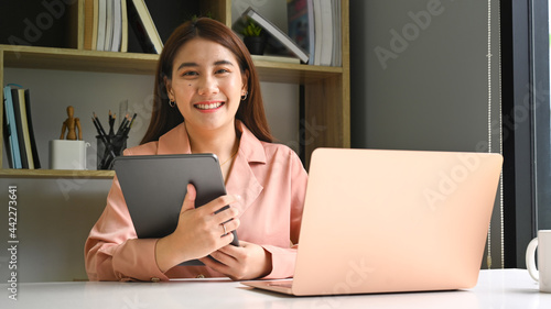 Attractive businesswoman holding digital table and smiling to camera.