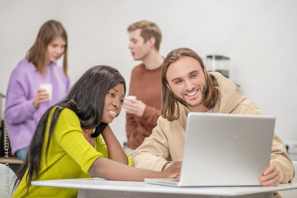 Darkskinned girl and caucasian guy interestedly looking at laptop Darkskinned girl and caucasian guy interestedly looking at laptop