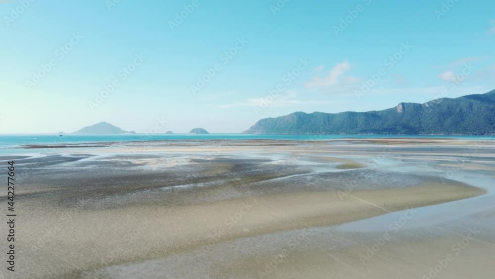 A tropical island in southeast Asia with a coastal area during a low tide. People are walking by the intertidal zone. The man is driving a motorbike on the sandy beach A tropical island in southeast Asia with a coastal area during a low tide. People are walking by the intertidal zone. The man is driving a motorbike on the sandy beach