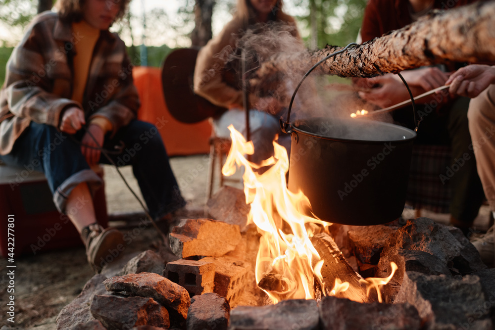 Fototapeta premium Close-up of food preparing in a pot on a fire with people sitting in the background