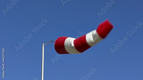 Windsock flutters in a strong wind showing wind direction and speed against perfect blue sky on clear summer day.