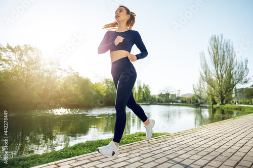 Athletic fit young woman jogging early in the morning in park