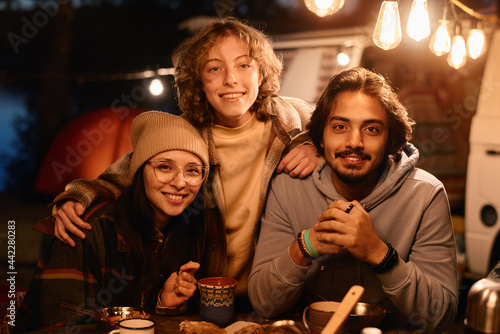 Portrait of friends smiling at camera while sitting at the table with food on a picnic outdoors
