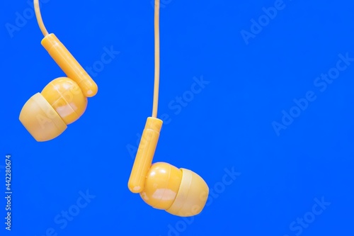 Foto Orange colored earbuds closeup on plain blue background with copy space