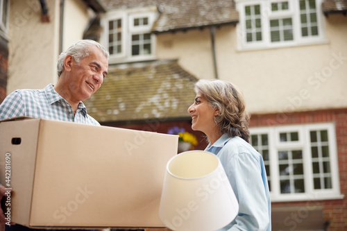 Mature Couple Carrying Boxes On Moving Day In Front Of Dream Home photo