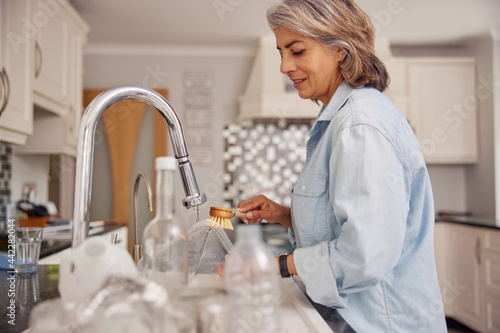 Mature Woman At Home In Kitchen Washing Used Packaging  Before Recycling photo