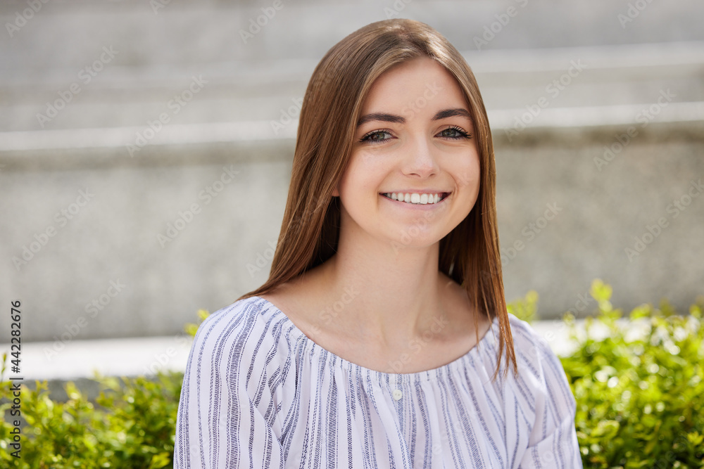 Portrait Of Smiling Young Woman Student Sitting Outside On College Campus