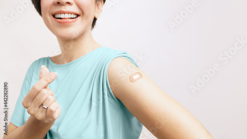 Vaccinated fighting against COVID-19 concept. Close up of a beautiful young asian woman show a band aid on her arm, make a mini heart and smiling. First dose vaccine, Recommended, Campaign, Insurance.