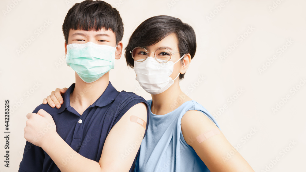 Global vaccination race against Covid 19 concept. Portrait of healthy young mother and teenager son with face mask show band aid on arms from first dose vaccine injection. Heard immunity campaign.